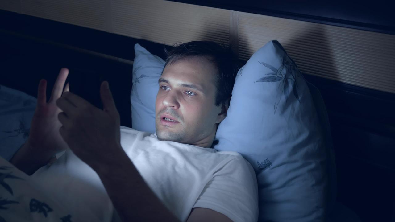 Homem usando celular na cama, antes de dormir