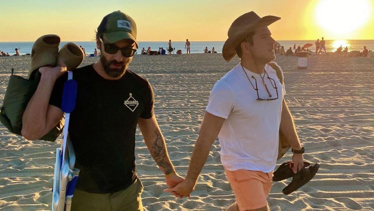 Ator Marco Pigossi e cineasta Marco Calvani de mãos dadas em praia