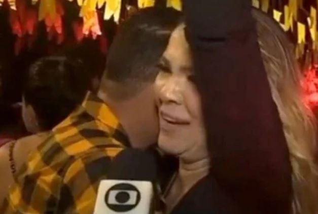 Homem parece esconder a face enquanto a mulher com quem dança dá uma entrevista.