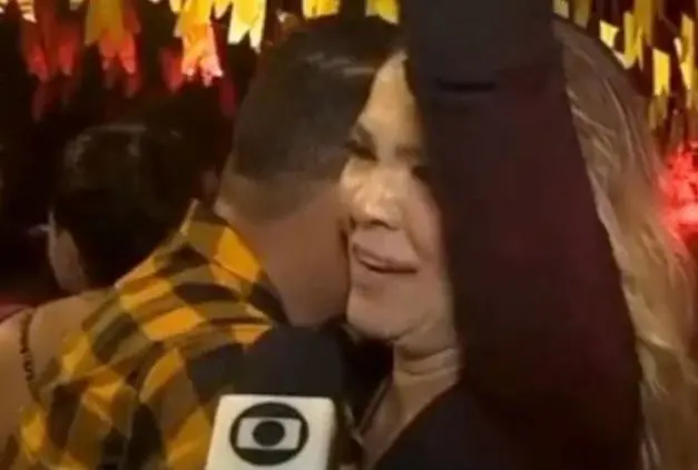 Homem parece esconder a face enquanto a mulher com quem dança dá uma entrevista.
