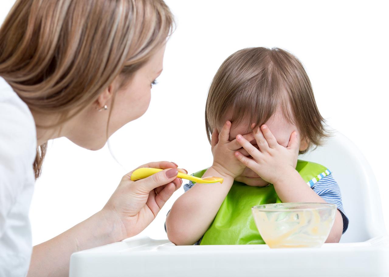 Criança em cadeirinha com mão nos olhos para não comer mais