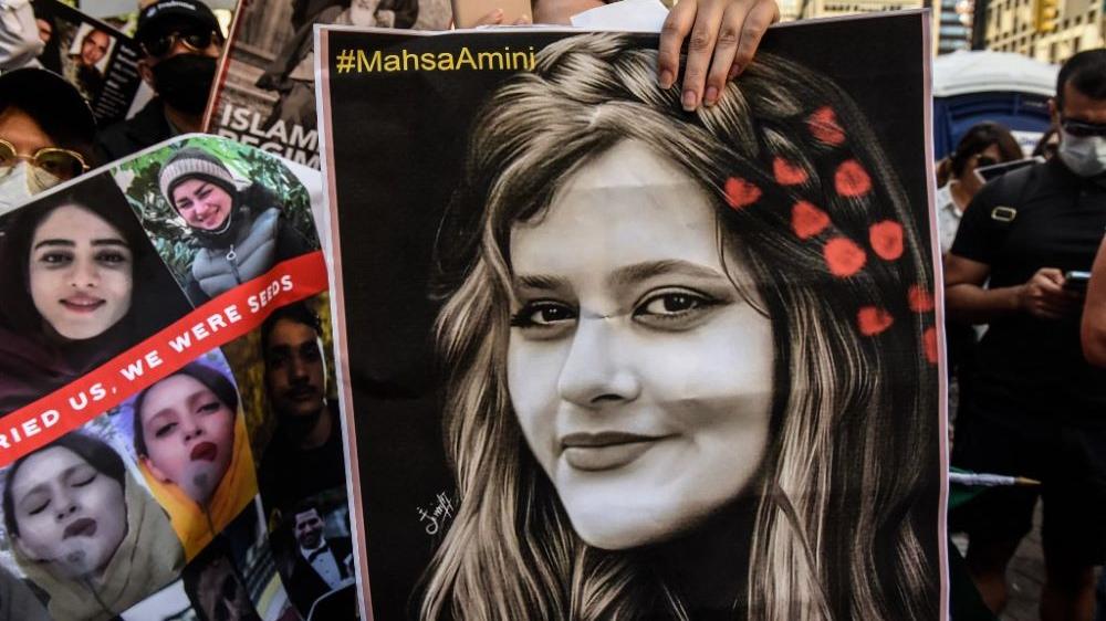 manifestante segura cartaz com a imagem da jovem Mahsa Amini durante protesto