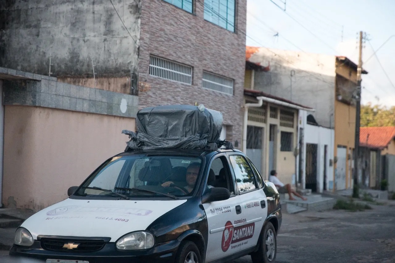 Na comunidade Sítio Córrego, o carro com alto-falante anuncia ofertas da farmácia enquanto um homem senta na calçada de casa