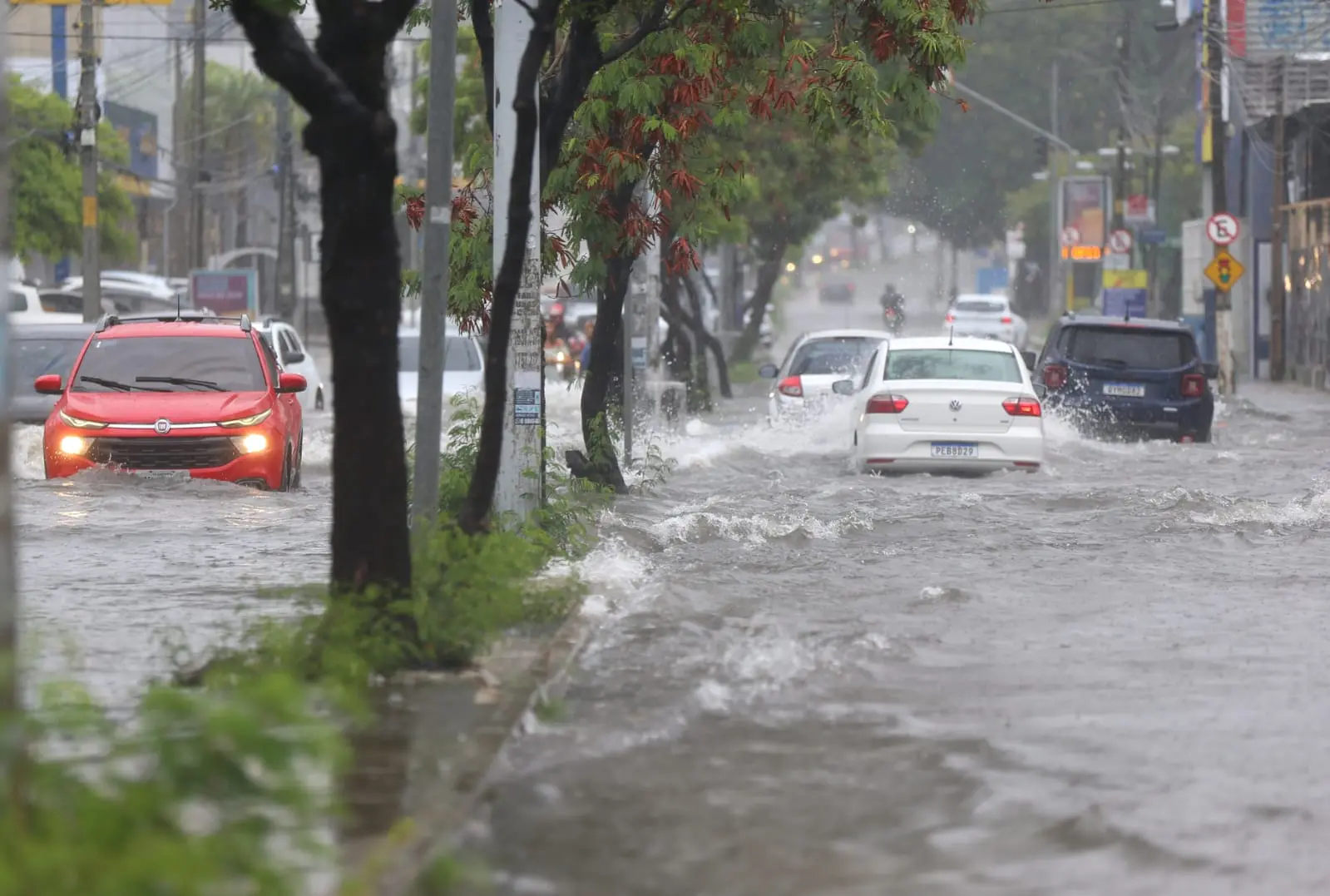 Carros trafegam por avenida alagada