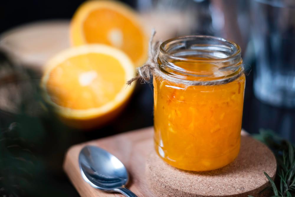 Geleia de laranja em vidro, ao lado de uma laranja cortada ao meio