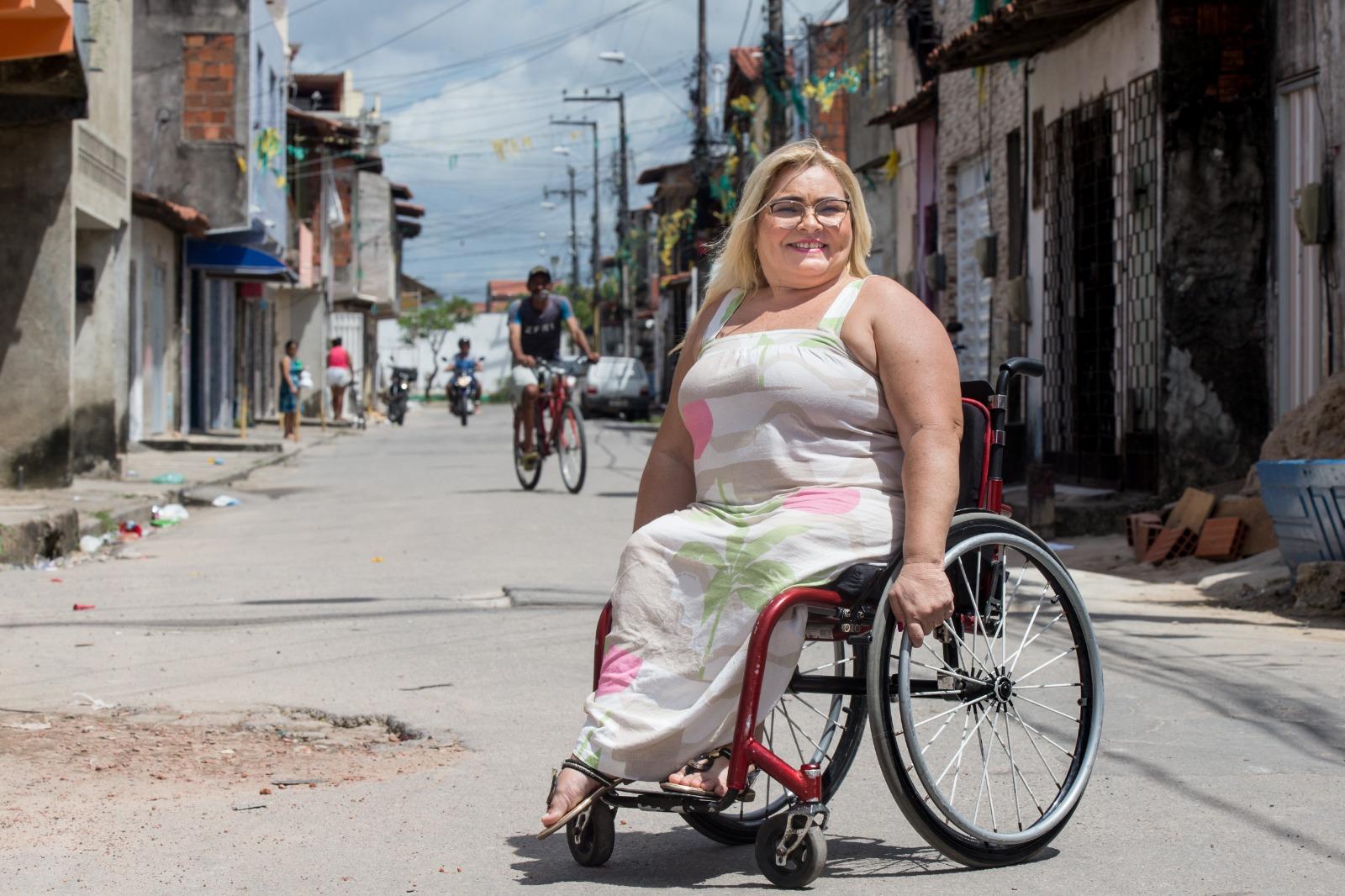 Mulher com deficiência física, em uma cadeira de rodas, em rua esburacada