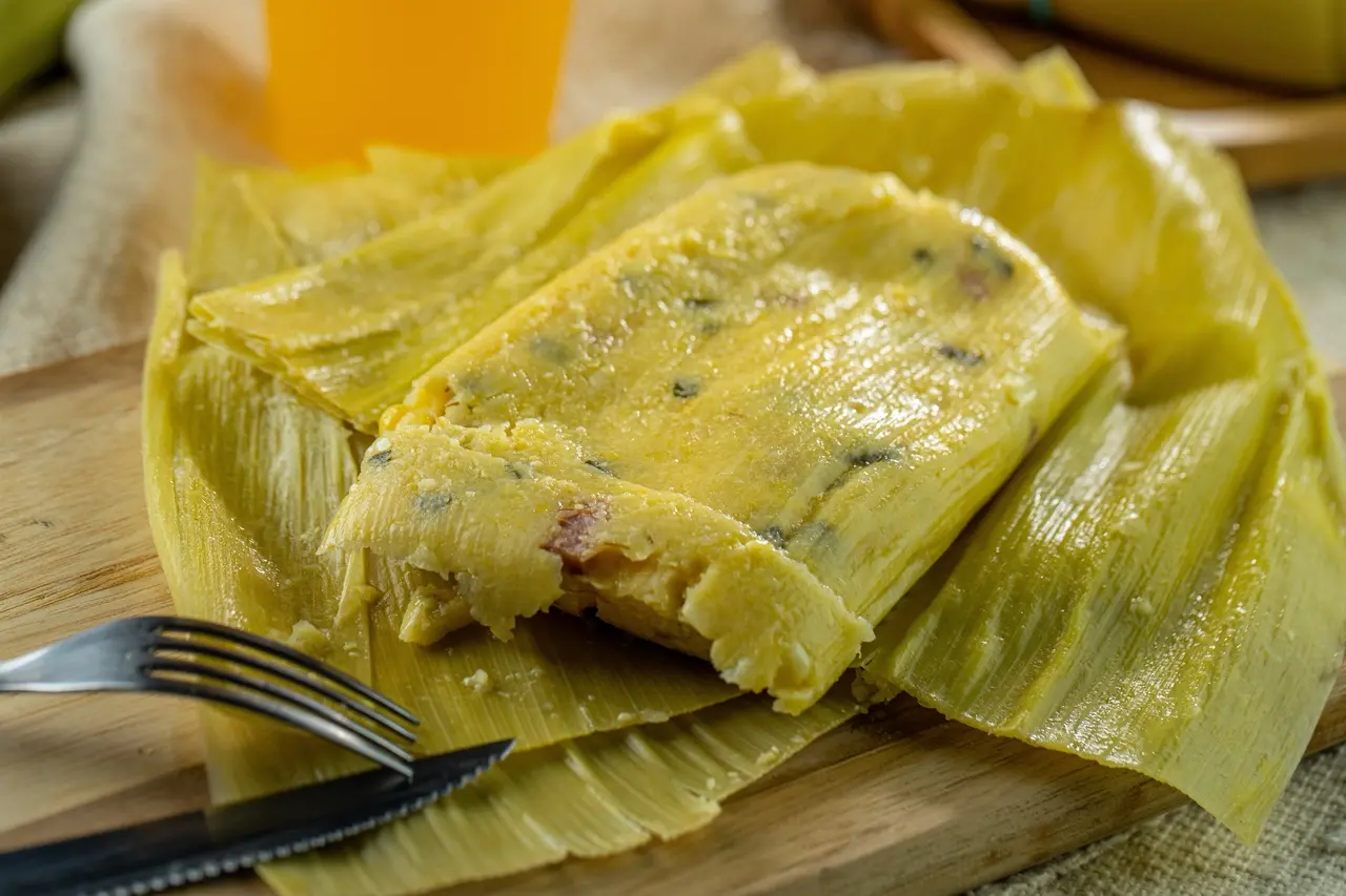 Pamonha em palha ao lado de garfo e faca