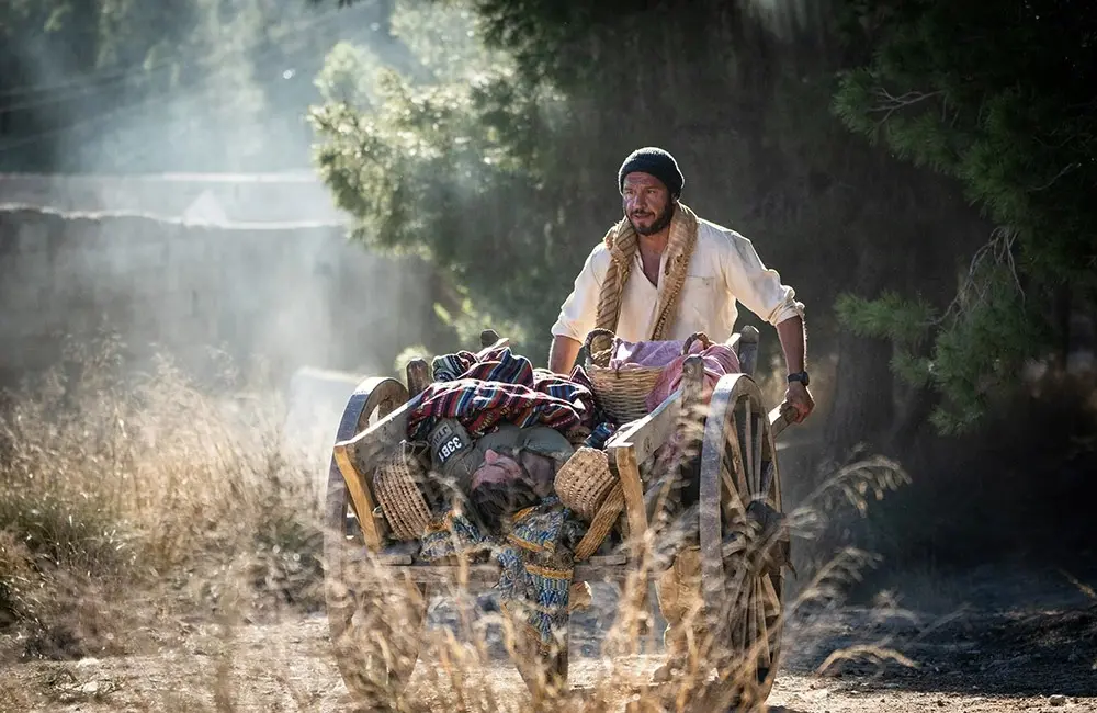 Homem  de blusa branca empurra carroça com soldado americano ferido