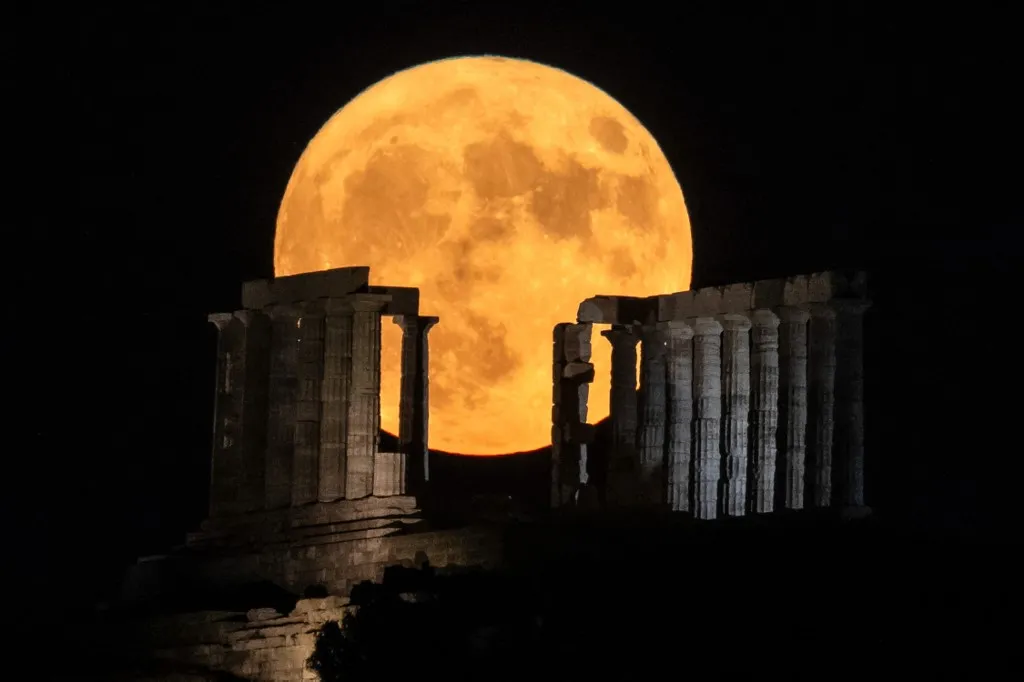 A lua registrada atrás do antigo templo de Poseidon no cabo Sounion, ao sul de Atenas