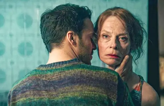 Homem jovem, branco de barba abraça mulher idosa, branca e com cabelos presos em um quartro