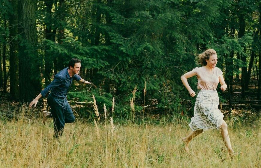 Homem e mulher jovens correm em meio a uma floresta como se estivessem brincando