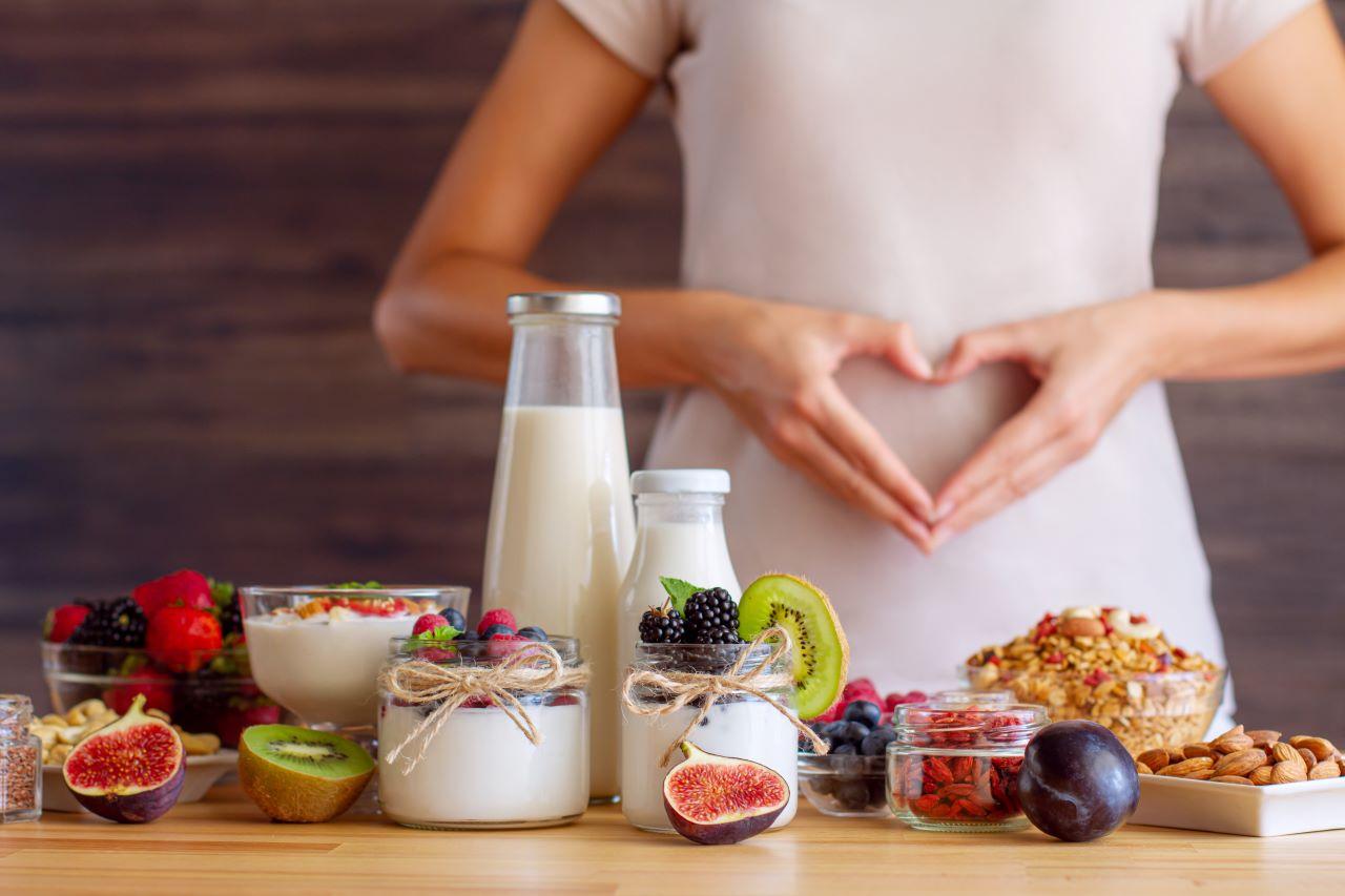 alimentos saudáveis sobre mesa diante de mulher com mãos sobre a região abdominal