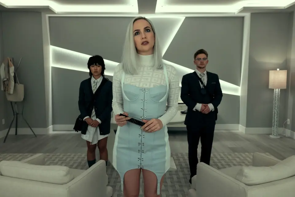 Mulher branca e loura aparece ao lado de um jovem casal oriental vestido com terno e gravata