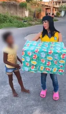 Kérollen Cunha entregando presente a criança negra. Influencers que deram banana e macaco de pelúcia para crianças são indiciadas por racismo