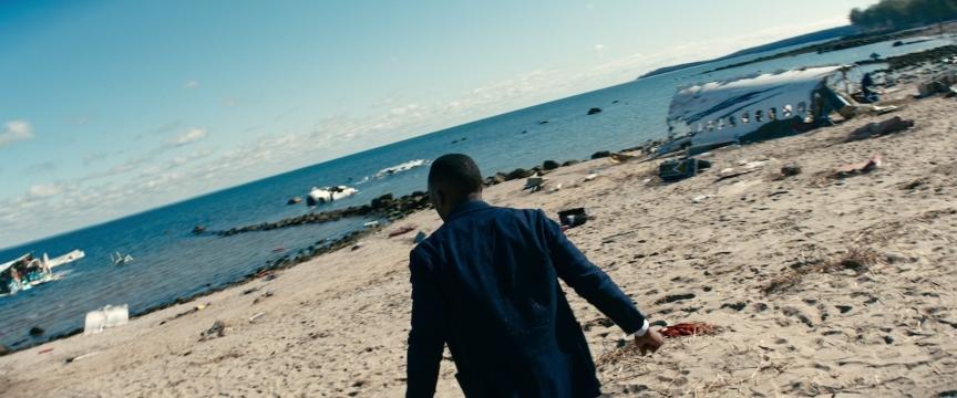 Homem negro aparece de costas olhando para a praia que está cheia de destroços