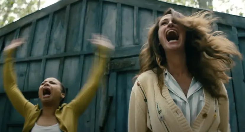 Duas mulheres acenam com expressão de medo em meio a uma floresta