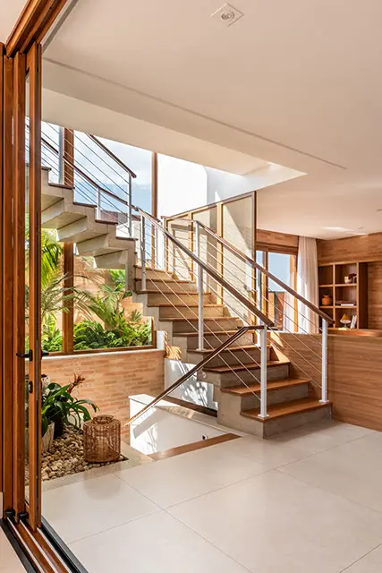 Estrutura da escada em L foi erguida em concreto armado com o piso revestido em madeira cumaru, tal qual o apoio do corrimão engendrado em ferro pintado de branco