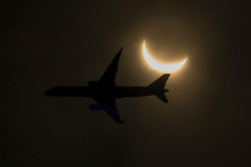 Imagem do eclipse solar com a silhueta de um avião em meio à penumbra