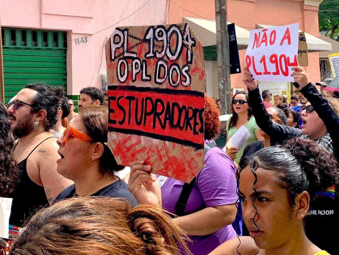 Concentração de manifestantes. Placas dizem: 'PL 1904, o PL dos estupradores' e 'Não ao PL 1904'