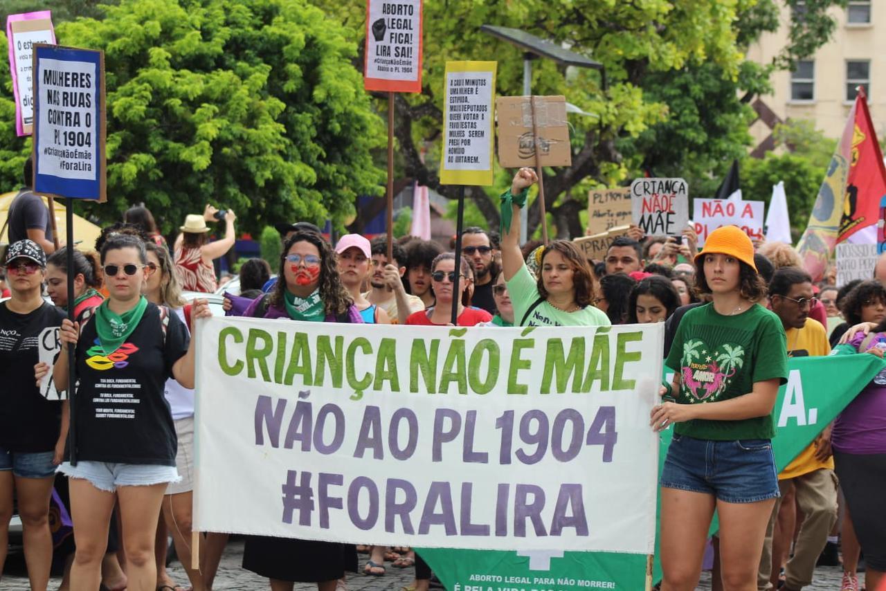 Manifestantes seguram placas contra o PL 1904. Faixa diz: 