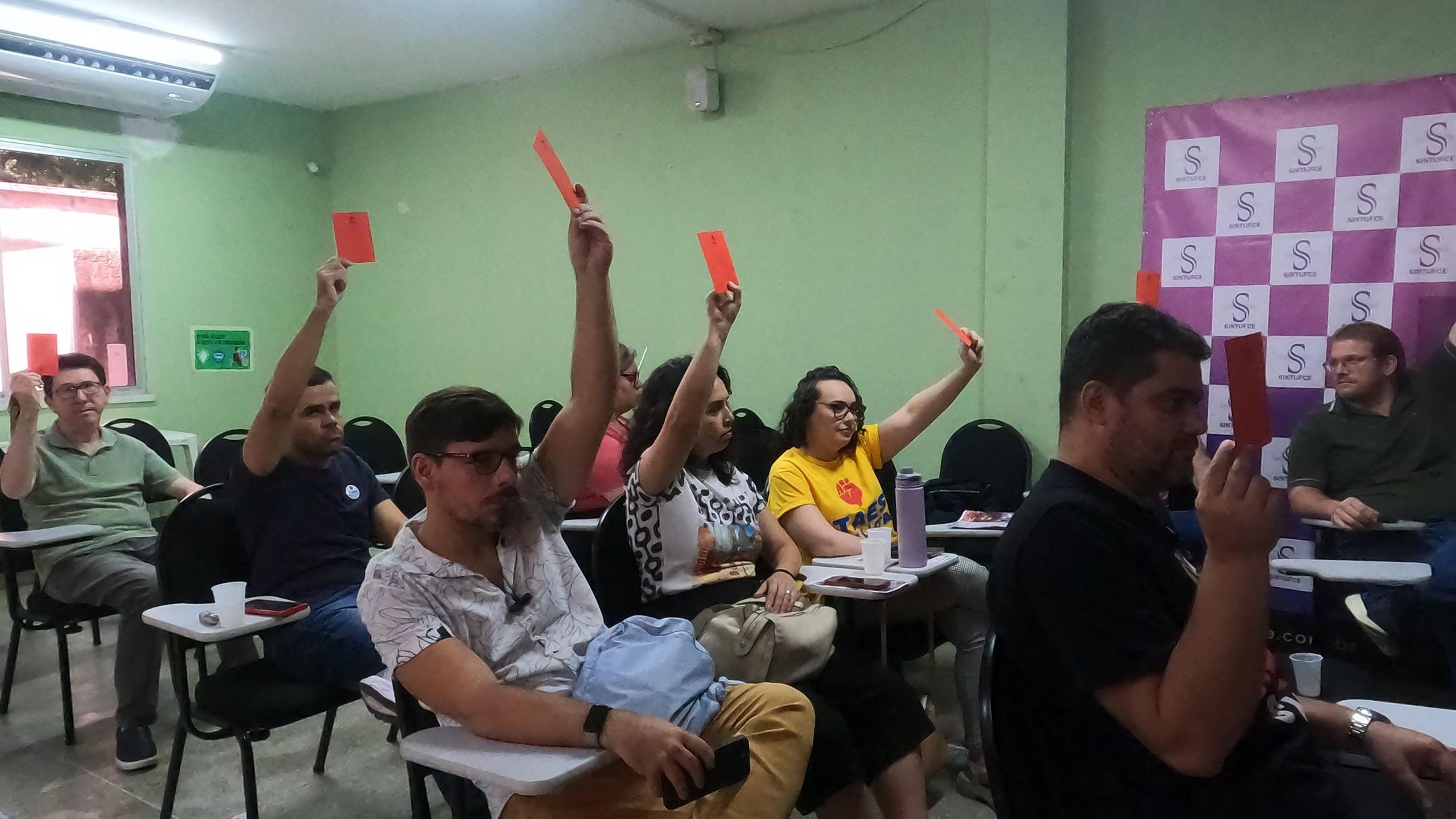 Servidores com uma mão para cima, levantando um cartão vermelho, votam pela continuidade da greve