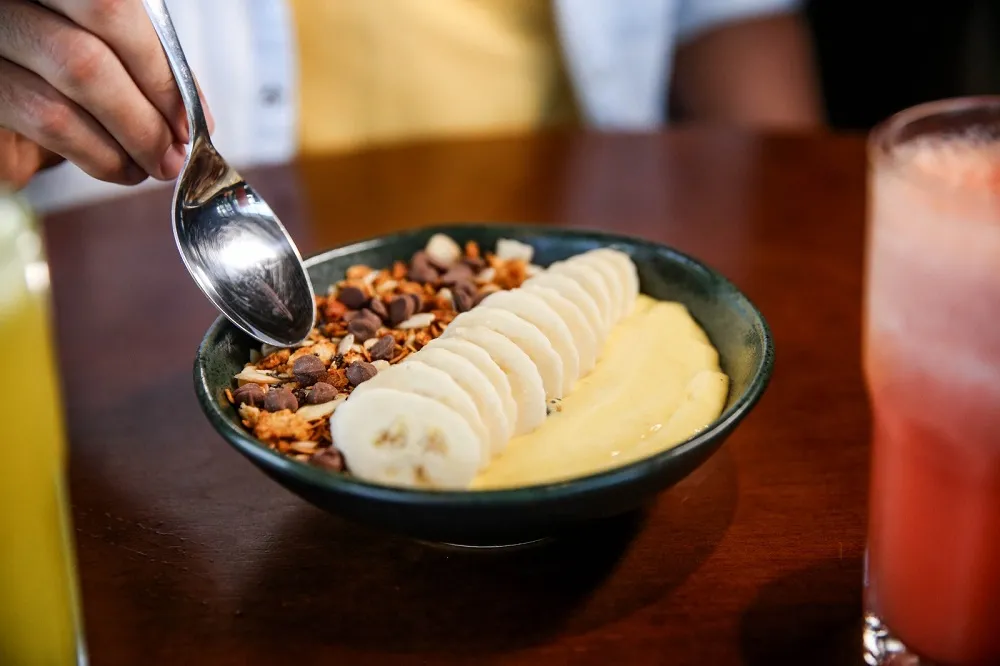 Delicioso, Smoothie de Manga traz a fruta batida com iogurte e tops de amêndoa, chocolate, granola e banana