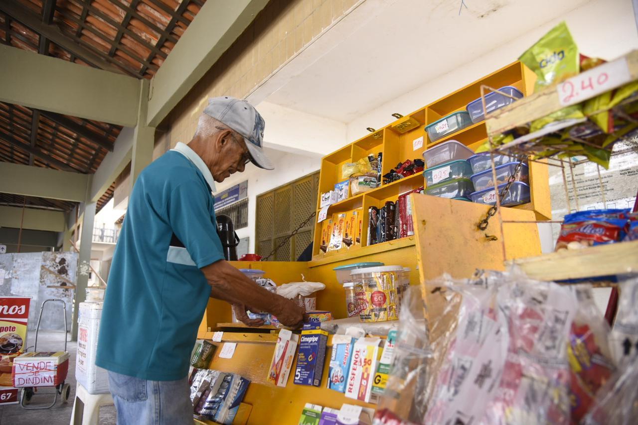 Idoso usando boné e óculos de grau organizando produtos da banca