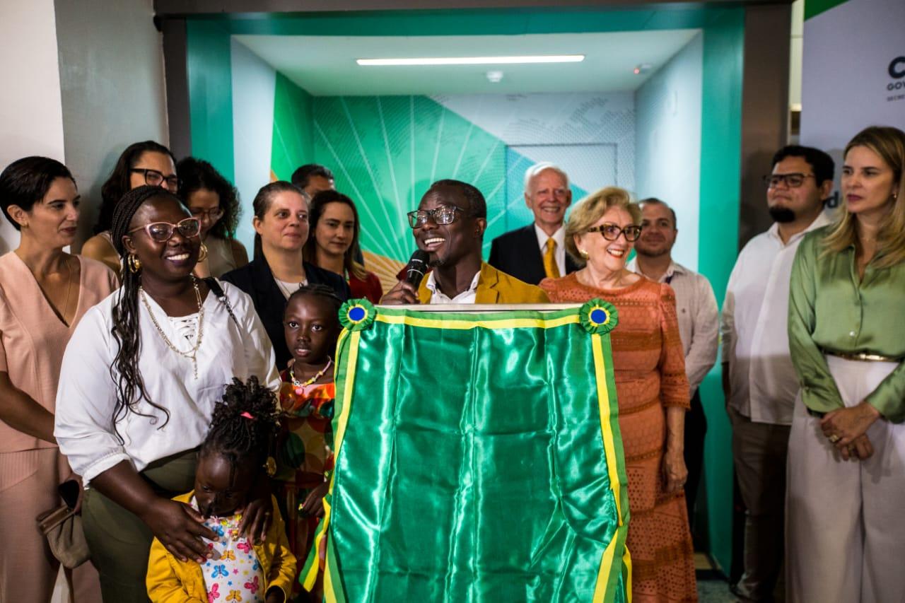 Pessoas ao redor da placa de inauguração do Posto Avançado de Atendimento Humanizado ao Migrante (PAAHM) instalado no Aeroporto de Fortaleza