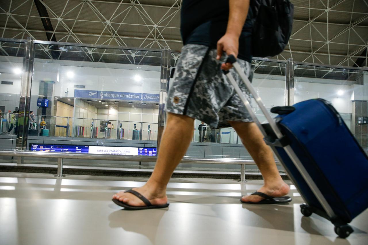 Passageiro andando no aeroporto de Fortaleza. A imagem foca nas pernas dele e na mala que ele carrega.