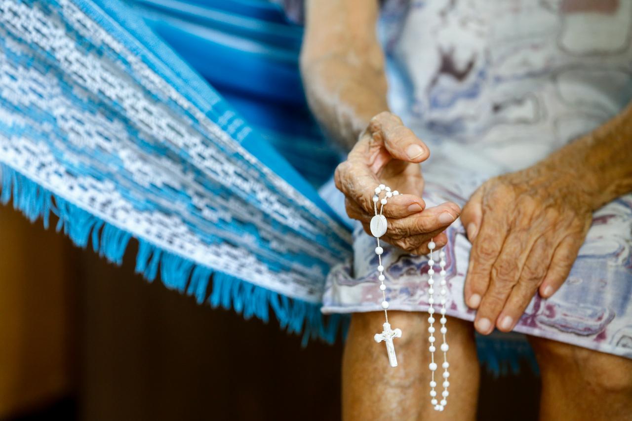 Mão de uma mulher idosa segurando terço