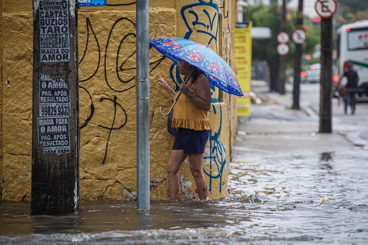 Imagem mostra pedestre andando por rua alagada durante chuva em fORTALEZA