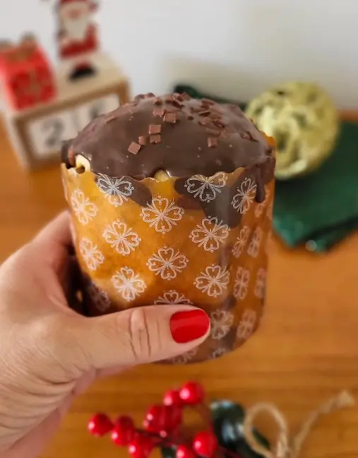 a imagem mostra uma pessoa segurando um mini panetone da loja Dona Açucarada com enfeites natalinos ao fundo