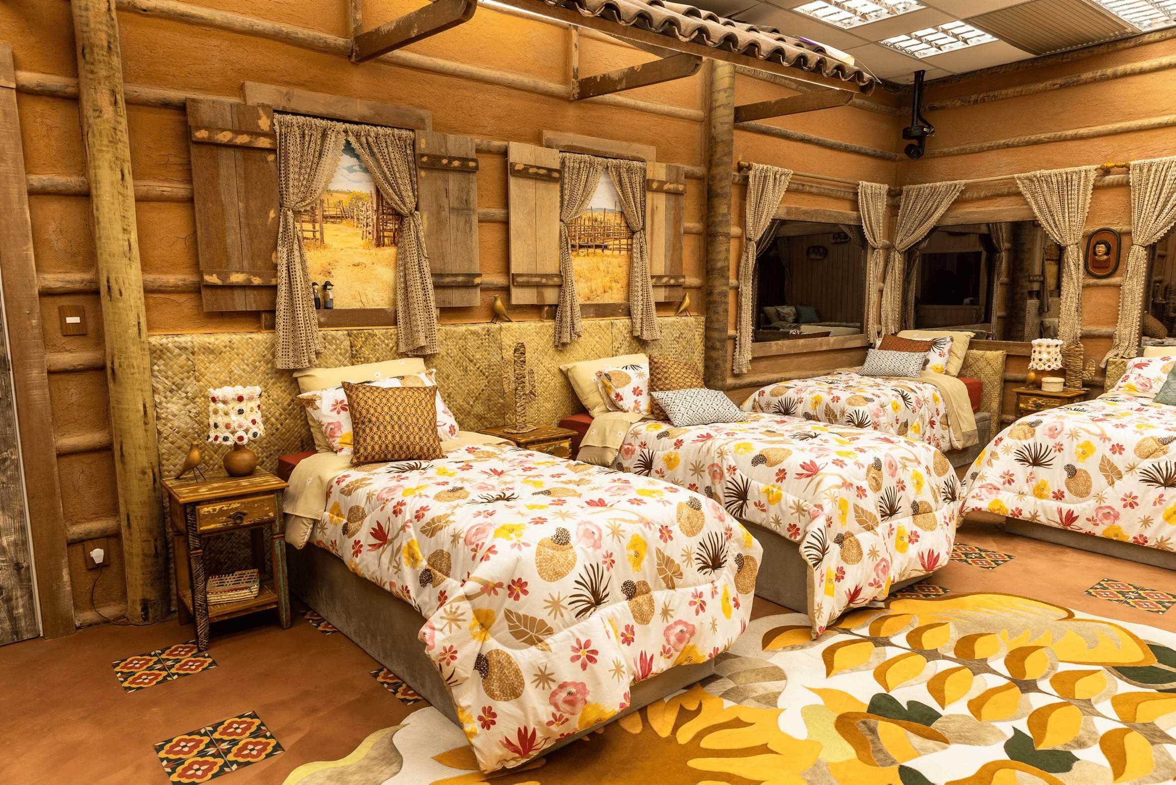 Quarto decorado com camas e roupas de cama florais, adornado com elementos rústicos e janelas com cortinas, oferecendo um ambiente aconchegante.