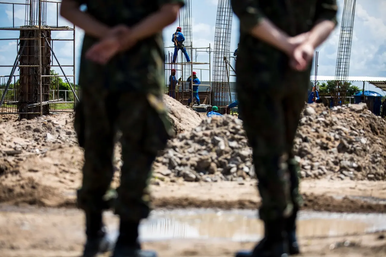 Em primeiro plano, dois militares estão desfocados, de costas para a foto, olhando os operários trabalhando na obra do ITA no Ceará