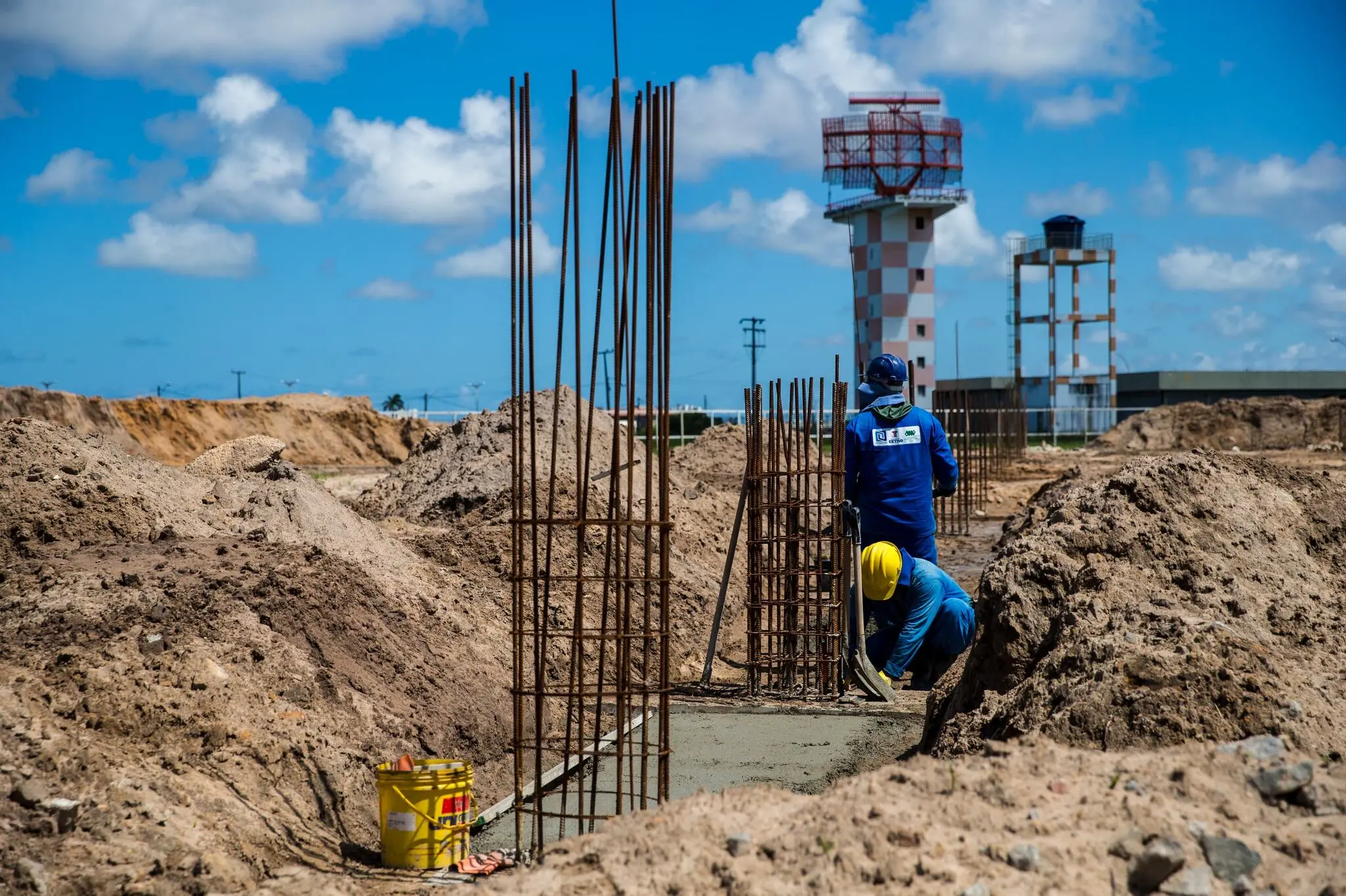 Área de construção com pilares metálicos em fase inicial, operários trabalhando