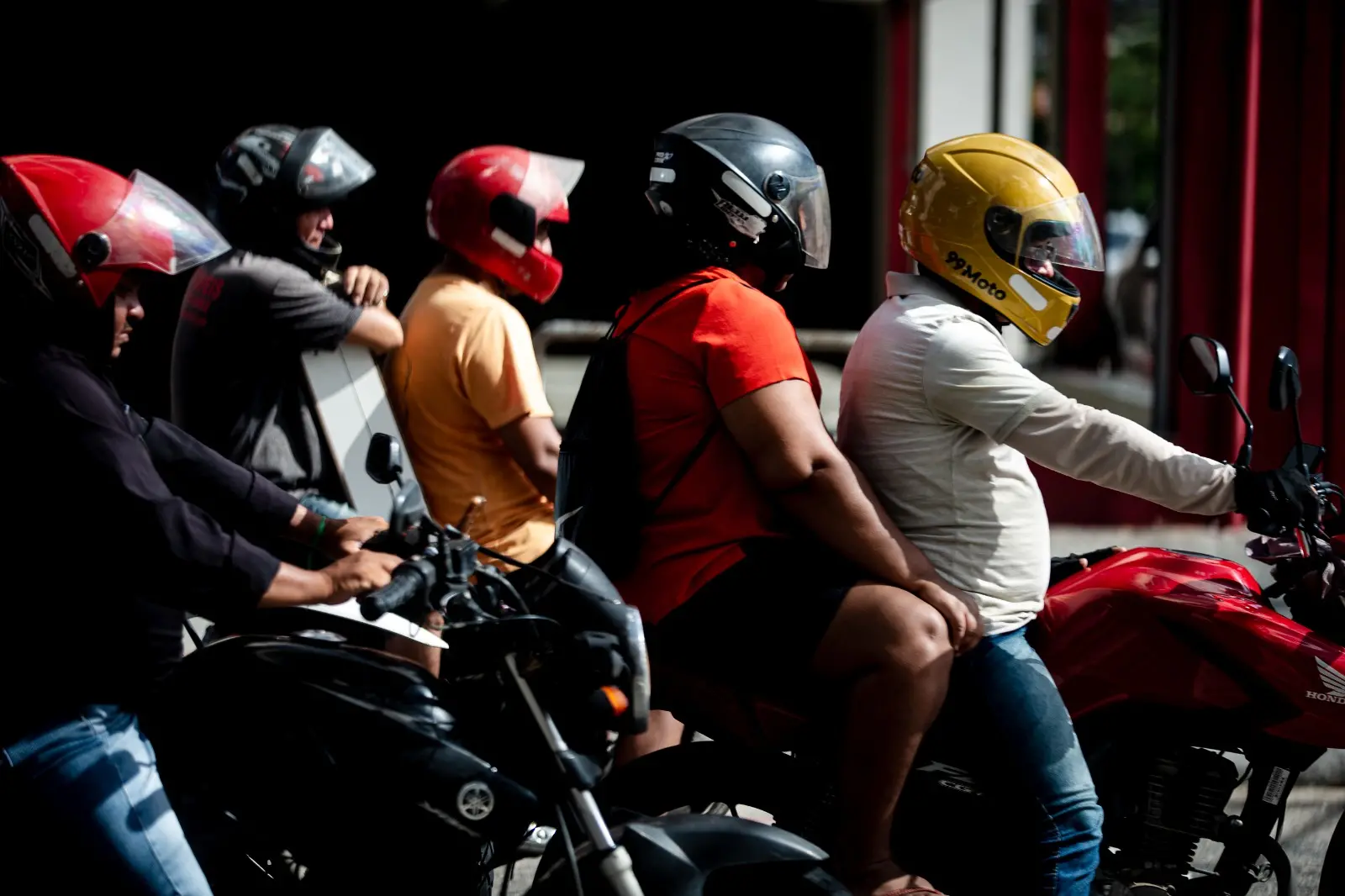 Três motociclistas e dois passageiros em uma rua de Fortaleza, esperando o sinal abrir