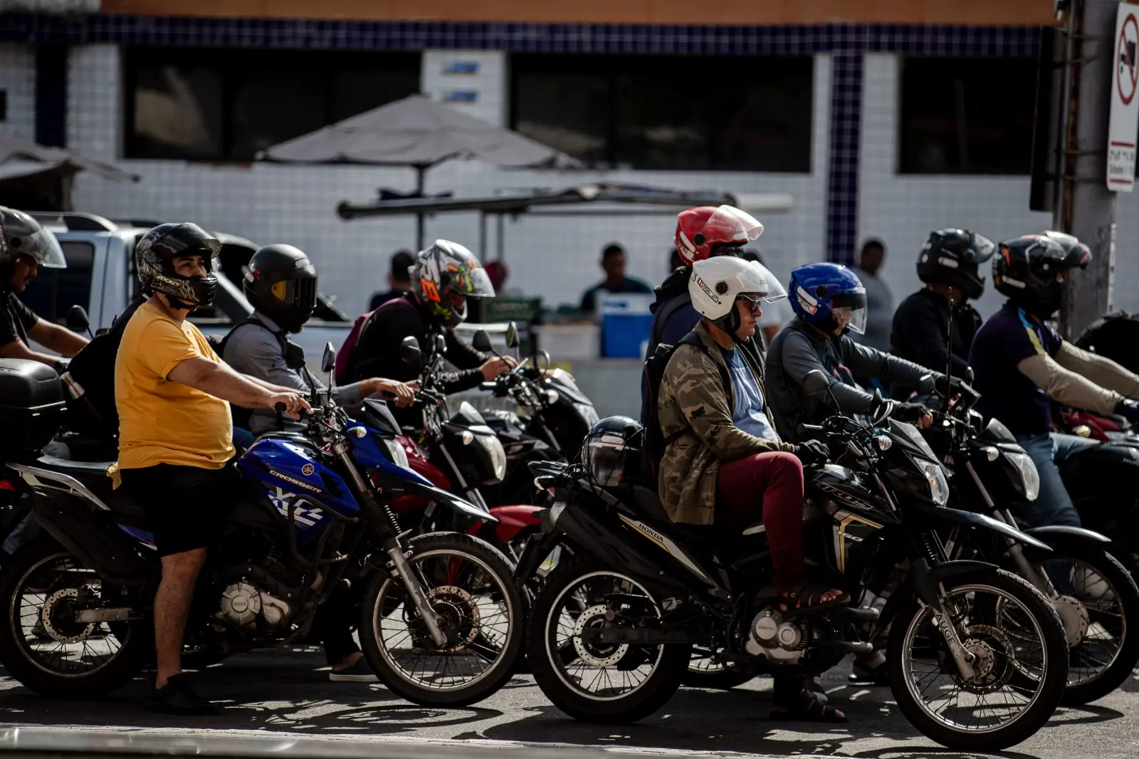 Vários motociclistas estão parados em uma avenida de Fortaleza, aguardando o sinal abrir
