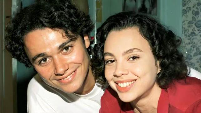 Imagem de um casal sorridente em um ambiente caseiro, com cabelos cacheados e expressões alegres.