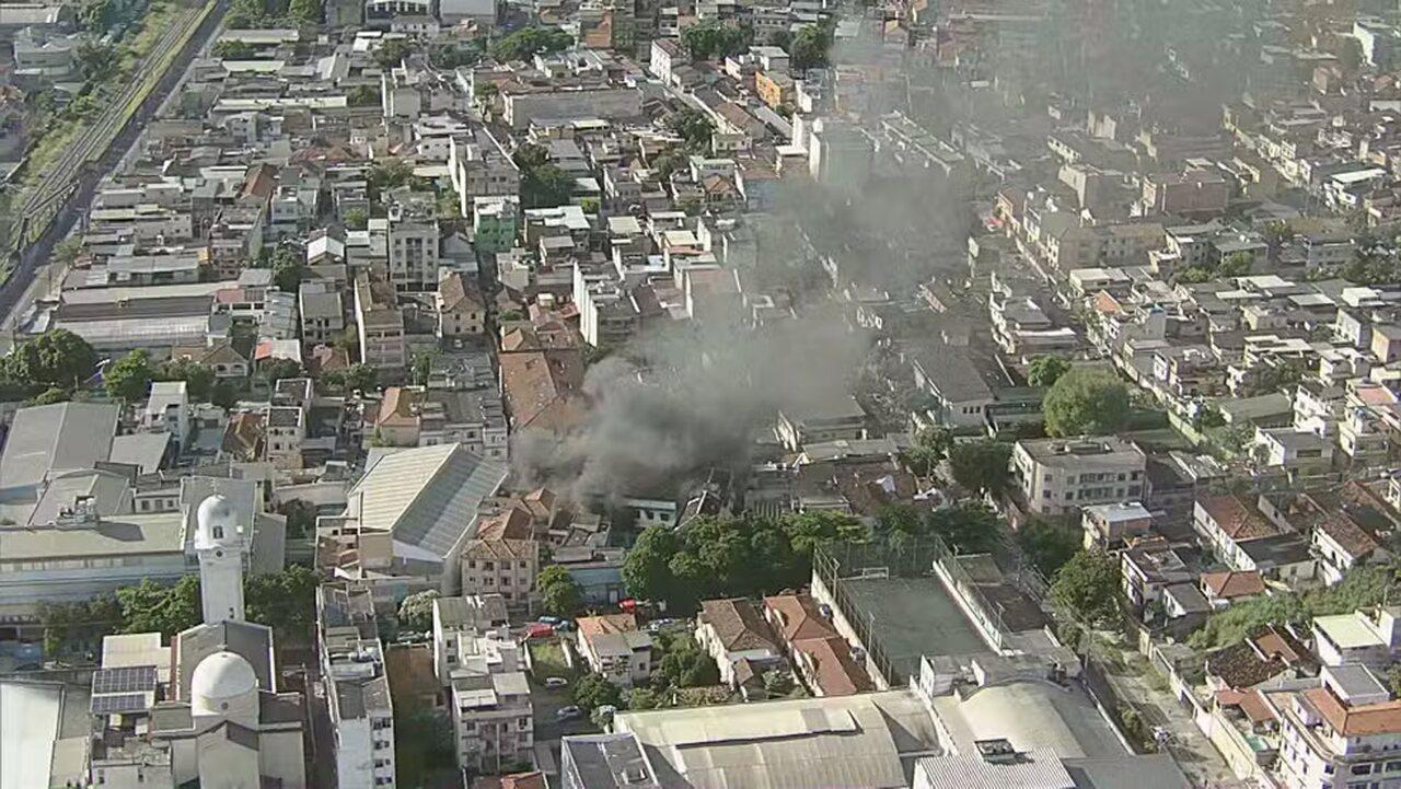 Vista aérea de uma área urbana mostrando fumaça saindo de uma edificação, em meio a um denso aglomerado de casas e estabelecimentos comerciais.