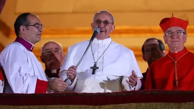 Foto do Papa Francisco dando seu discurso em público, cercado por cardeais e autoridades da Igreja Católica.