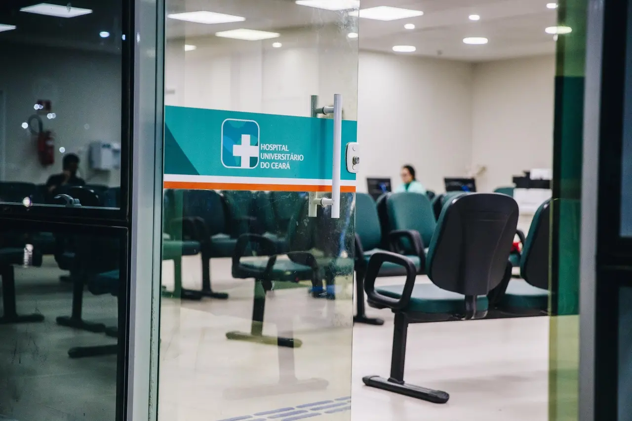 Recepção do Hospital Universitário do Ceará, com cadeiras verdes e portas de vidro