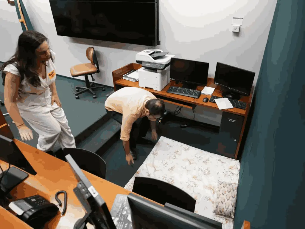 Glauber Braga (Psol-RJ) se abaixando para mexer em um colchão improvisado no chão e uma mulher branca de cabelos longos apoiada em uma mesa enquanto observa