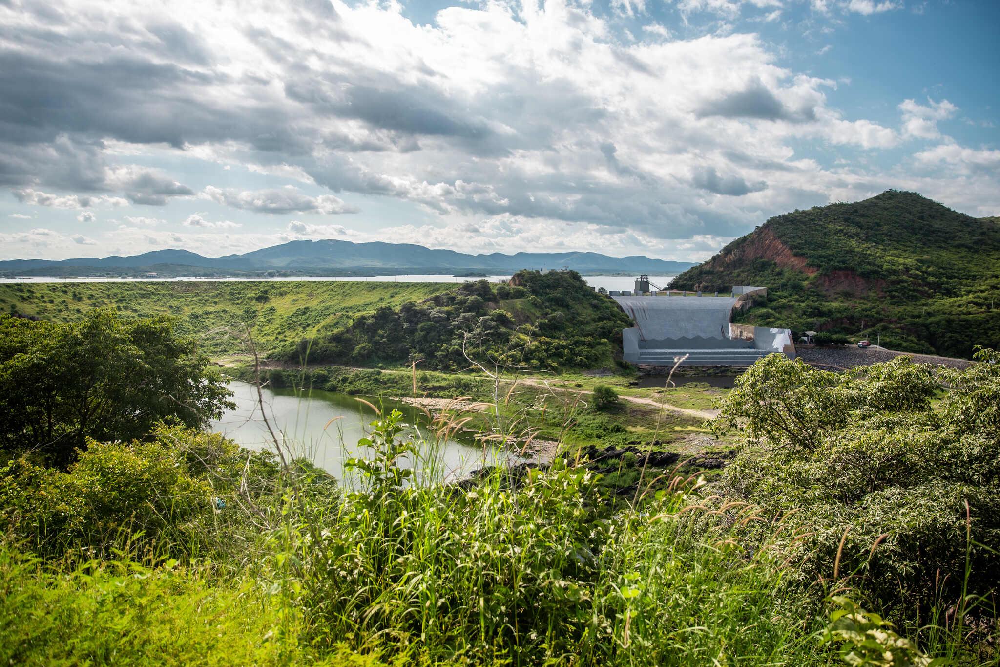 Vista da paisagem ao redor do açude Orós, com vegetação ao redor e a parede do sangradouro