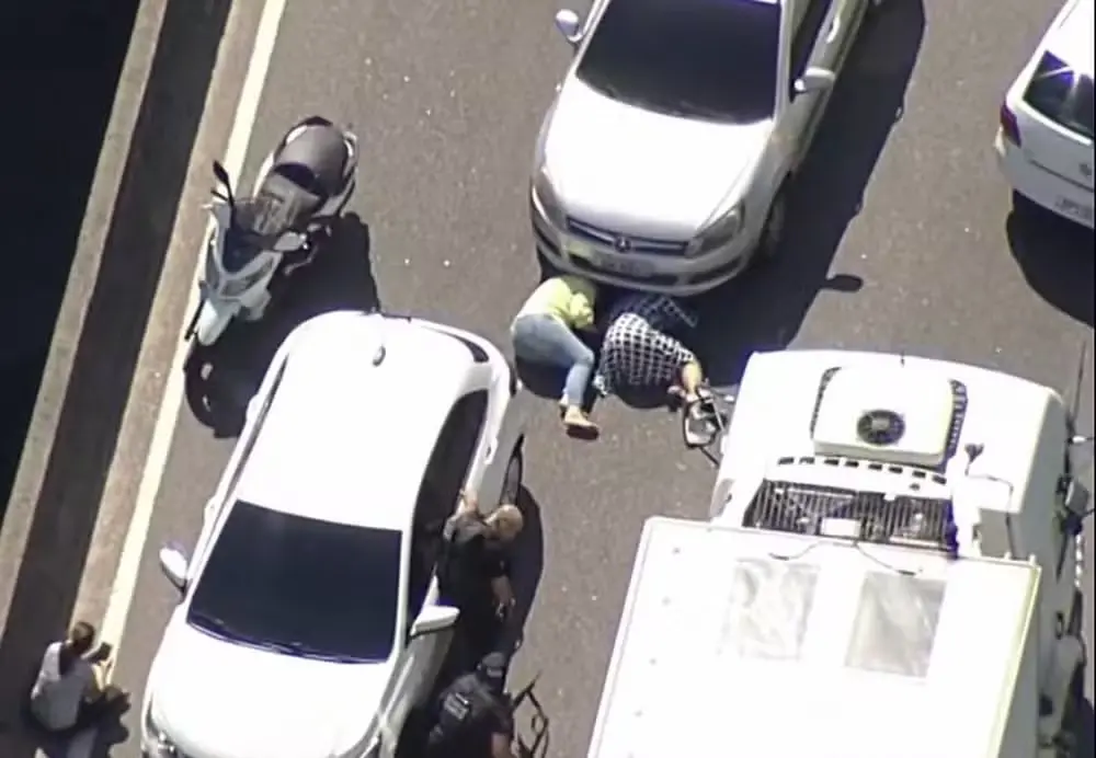 Imagem mostra motoristas e passageiros deitados no chão de uma avenida buscando proteção durante operação policial na Cidade de Deus