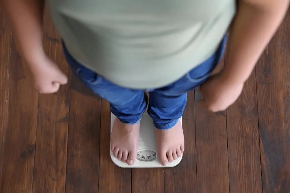 Imagem de visão superior de um adolescente com sobrepeso em pé em cima de uma balança para matéria sobre novos critérios para cirurgia bariátrica