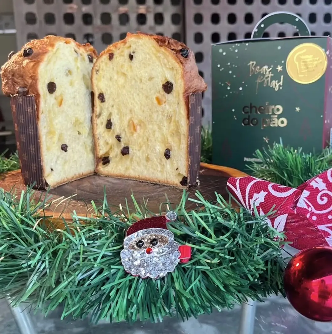Panetone da Cheiro do Pão recheado com frutas cristalizadas e gotas de chocolate, decorado com enfeites natalinos e uma decoração festiva ao redor.