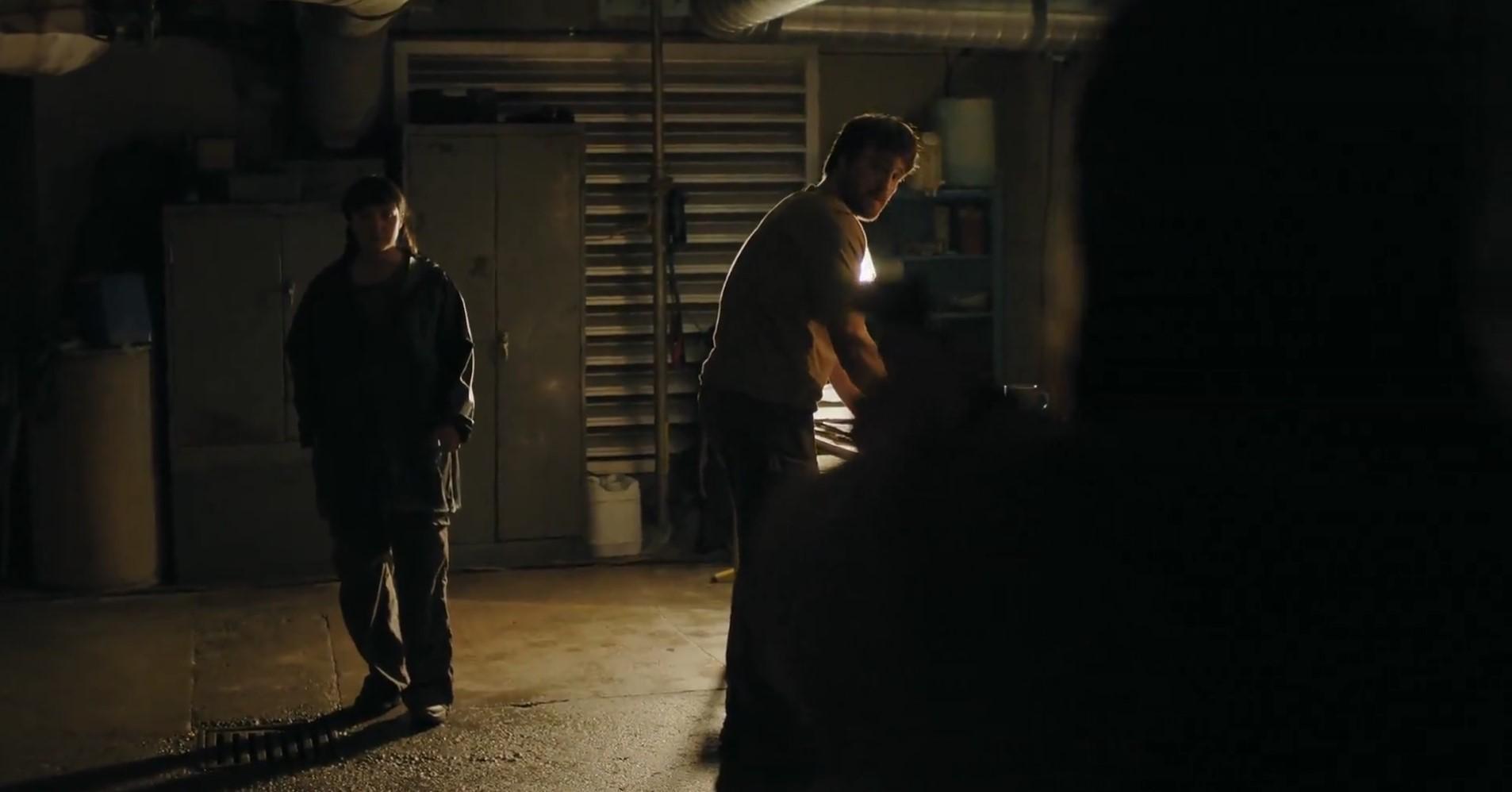 Cena dramática de Owen e Mel, de The Last of Us, em uma garagem escura, com iluminação fraca destacando suas silhuetas, expressão tensa e ambiente misterioso para matéria explicando se Ellie morre
