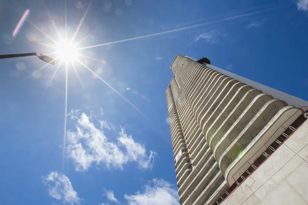 Imagem feita de baixo para cima mostra um prédio de altura bastante elevada em contrate com a luz solar