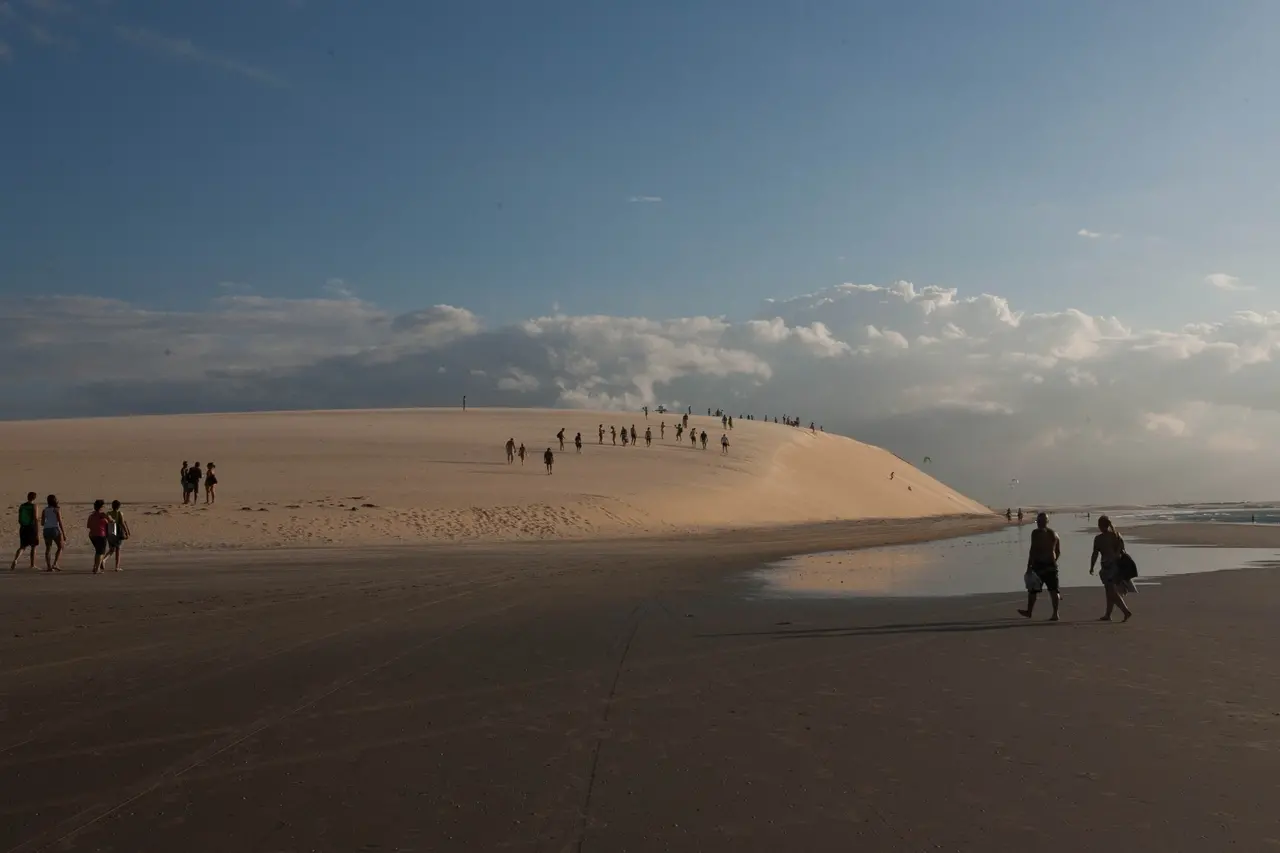 Imagem de duna em praia com várias pessoas no local