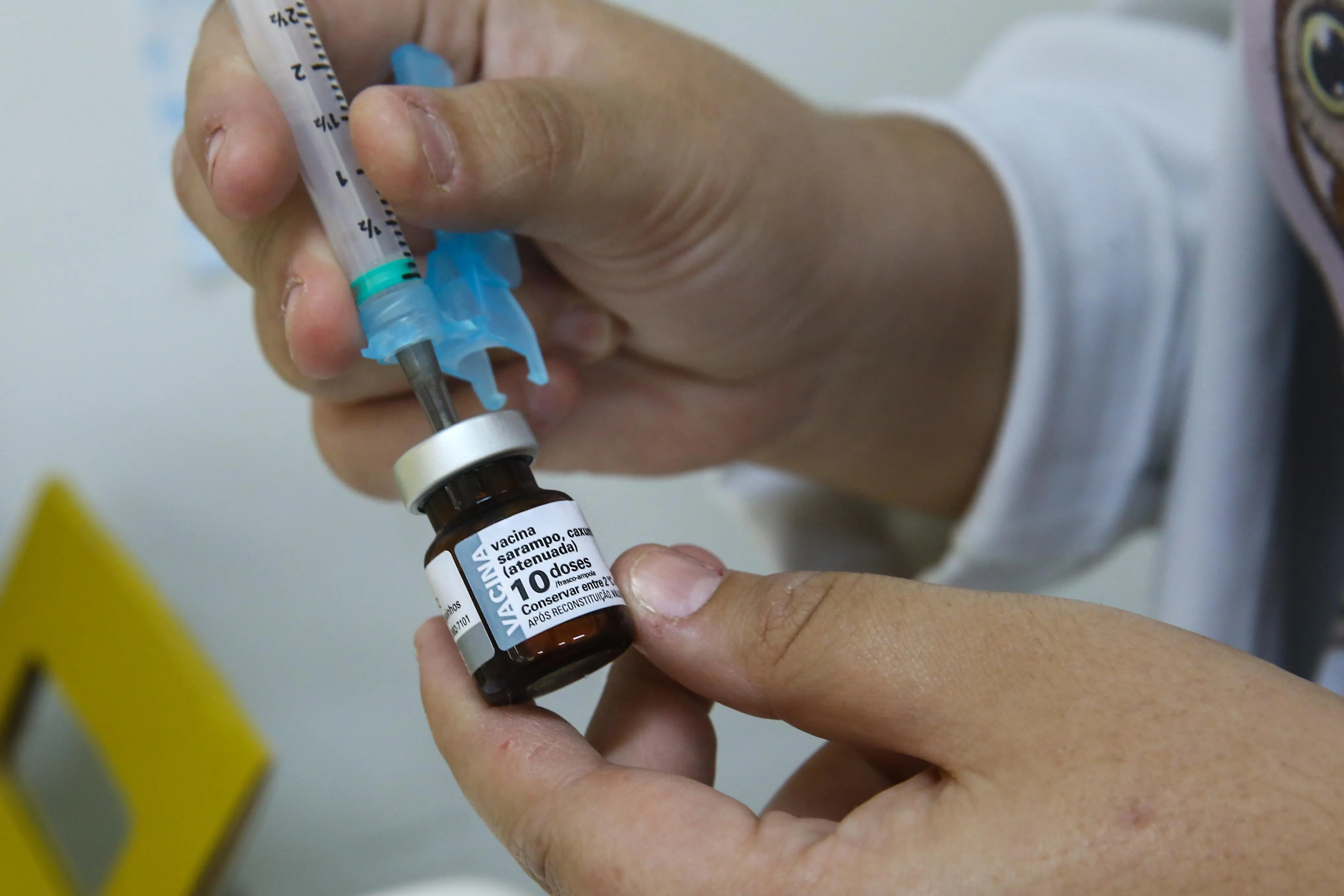 A foto mostra uma pessoa segurando um pequeno frasco de vidro rotulado 